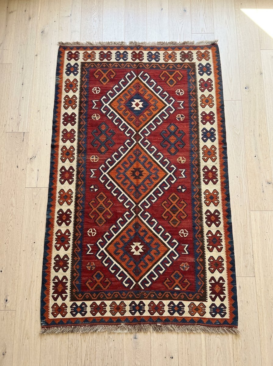 Red bohemian style rug with cream borders and diamond shapes on light hardwood flooring.