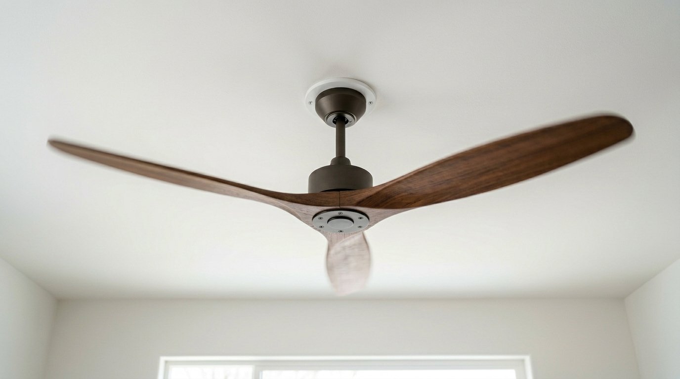 A low angle view of a contemporary three-blade wooden ceiling fan with a dark metal finish mounted on a white surface.
