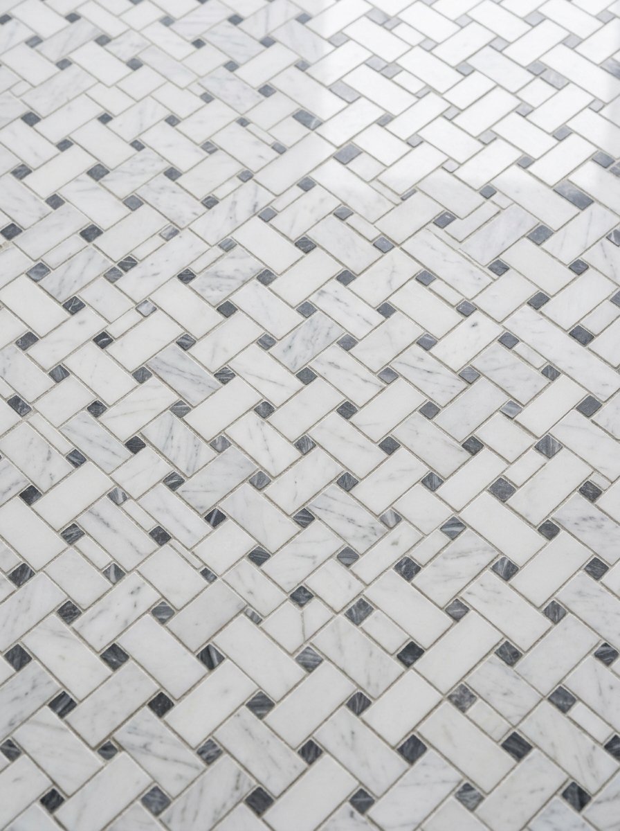 Close up of white marble basketweave tiles featuring small dark grey square stone inserts.