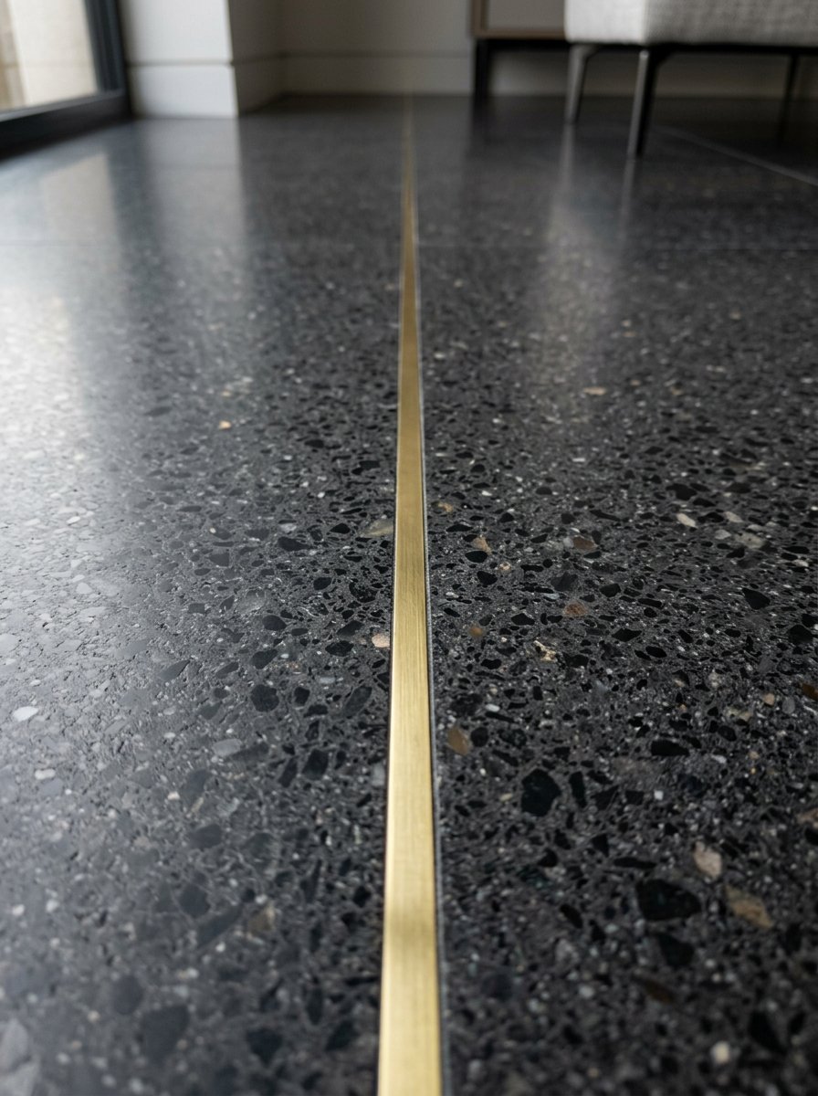 Close up of a metallic gold divider strip set into a sleek black stone floor with grey and white aggregate.