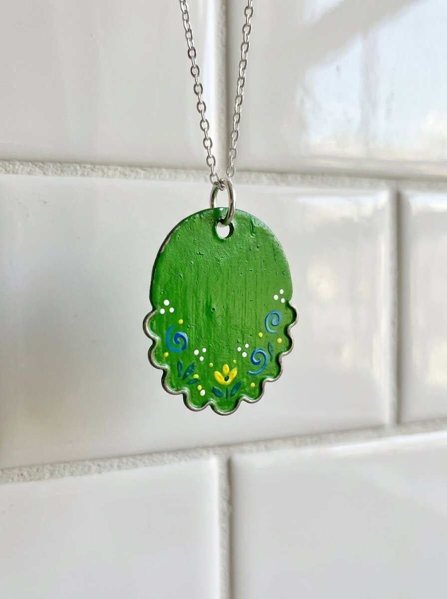Close-up of a scalloped-edge green pendant with small yellow and blue painted flowers on a silver chain.