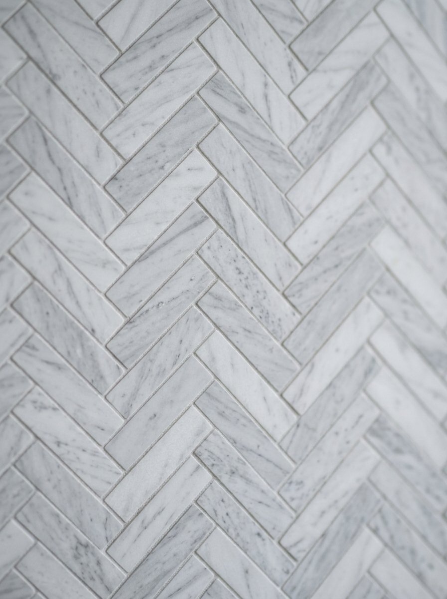 Textured white marble tiles arranged in a classic herringbone pattern with narrow grey grout lines.