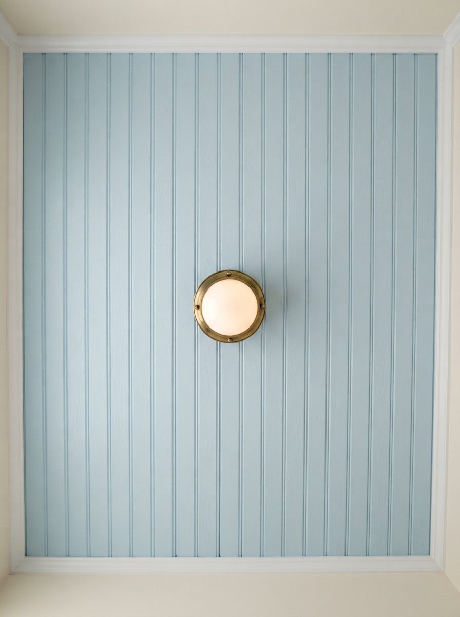 Round brass ceiling light centered on a light blue vertical wood panel ceiling with white trim.