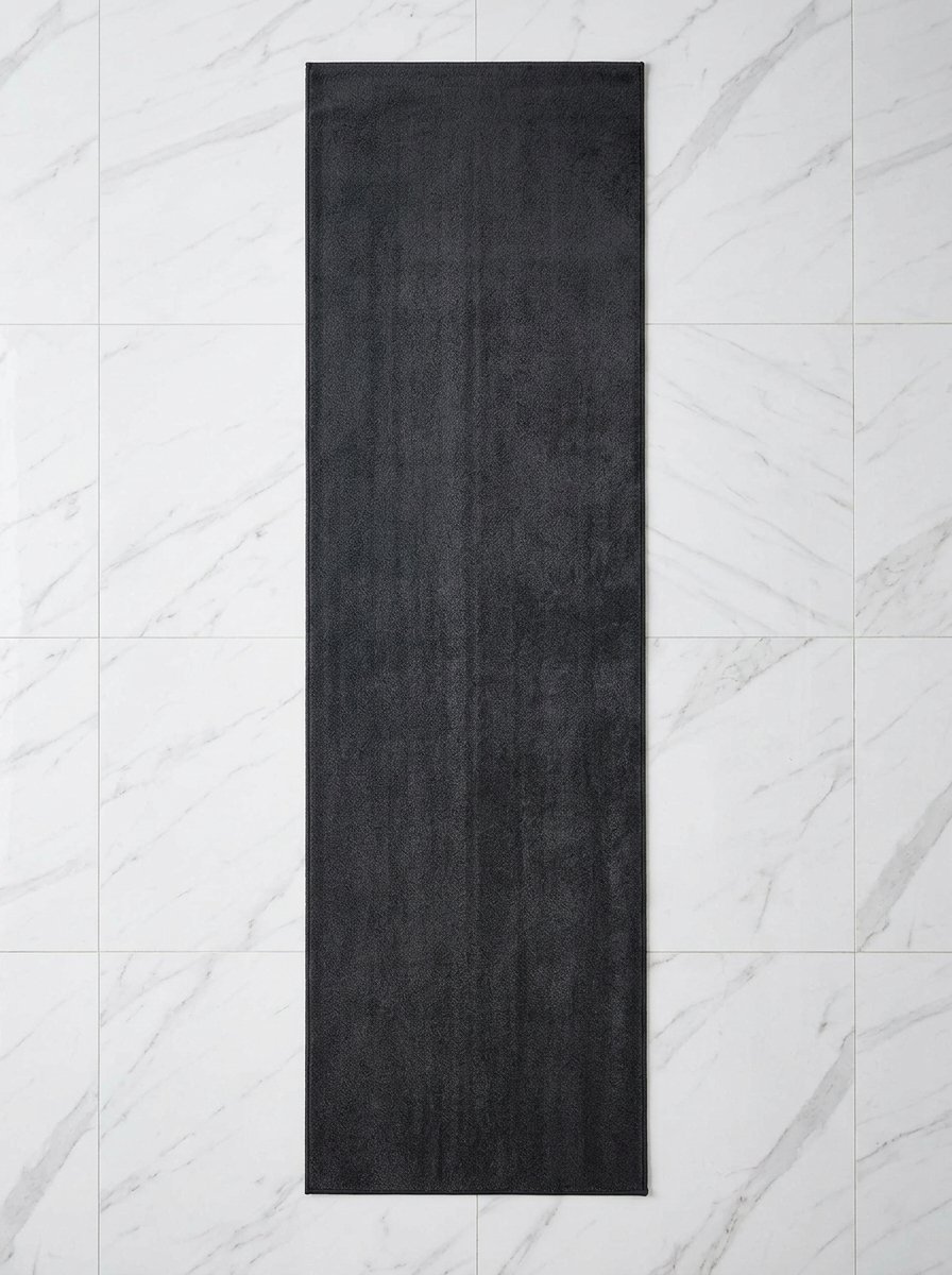 Top-down view of a soft black floor mat centered on bright white marble bathroom flooring.