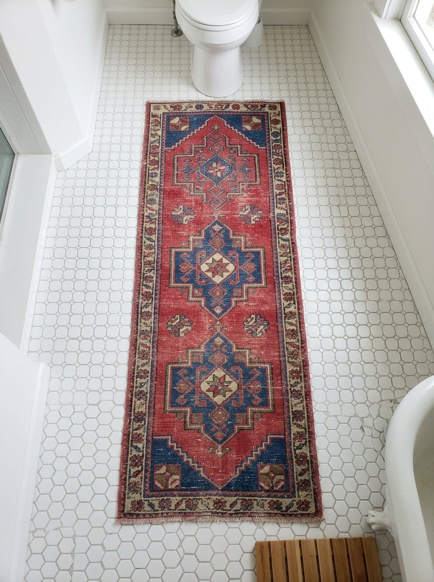 A long, decorative red and blue Persian-style rug placed on a white hexagonal tiled bathroom floor.